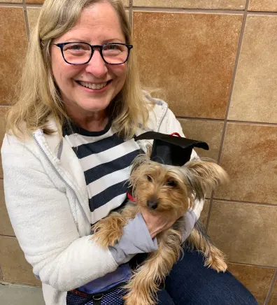 Sue's staff photo from Lifetime Animal Care Center where she is holding a puppy with a graduating cap on its head.